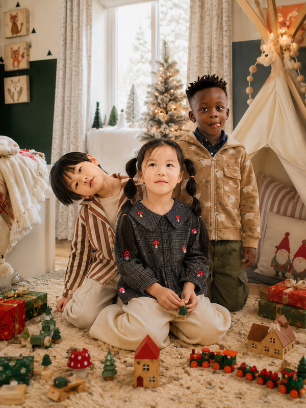 Girl in grey houndstooth mushroom top poses with siblings by Christmas tree - kids fall clothing