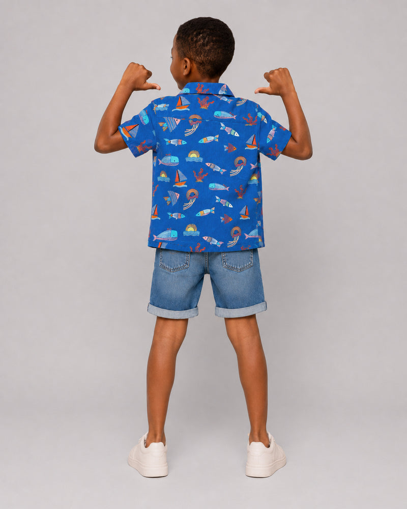 Boys ocean themed shirt in blue, sailboat and fish print, back view on model