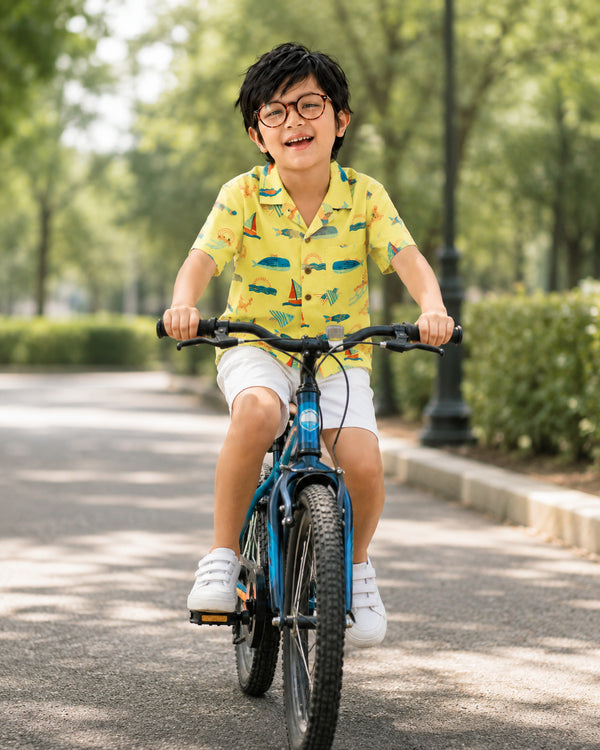 Young boy riding a bicycle in an ocean-print shirt and white shorts from Kissa beachwear for infants collection