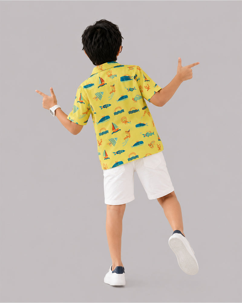Back view of boys ocean themed shirt in yellow, white shorts and sneakers