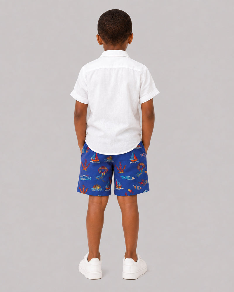 Boys ocean themed shorts in blue, sailboat and fish print, back view on model