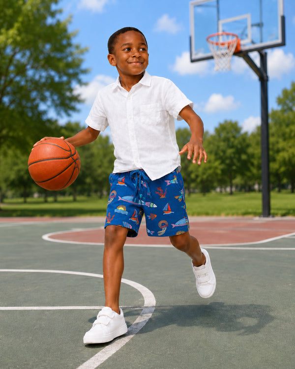 Young boy playing basketball wearing blue ocean-print shorts, part of Kissa beachwear for infants collection.