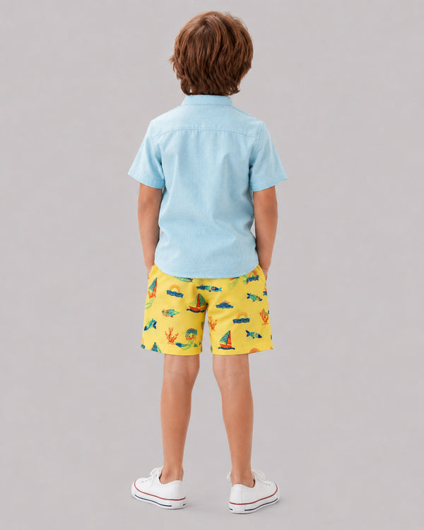 Boy wearing yellow ocean themed shorts with light blue shirt, back view