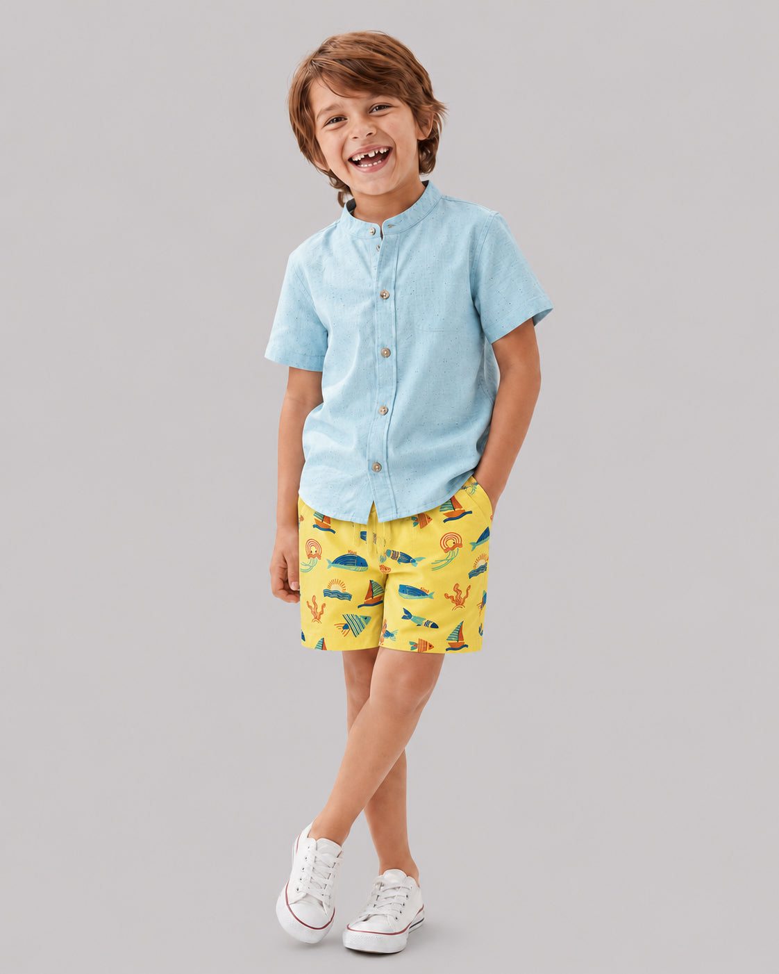 Boy in yellow ocean themed shorts and light blue shirt, smiling, front view