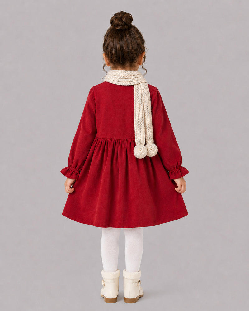 Girl in red corduroy dress and cream pom scarf, a cozy pick among Kissa's dresses for girls