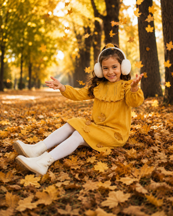 Girl playing in fallen leaves wearing mustard yellow ruffle dress, a cozy fall dresses for girls pick