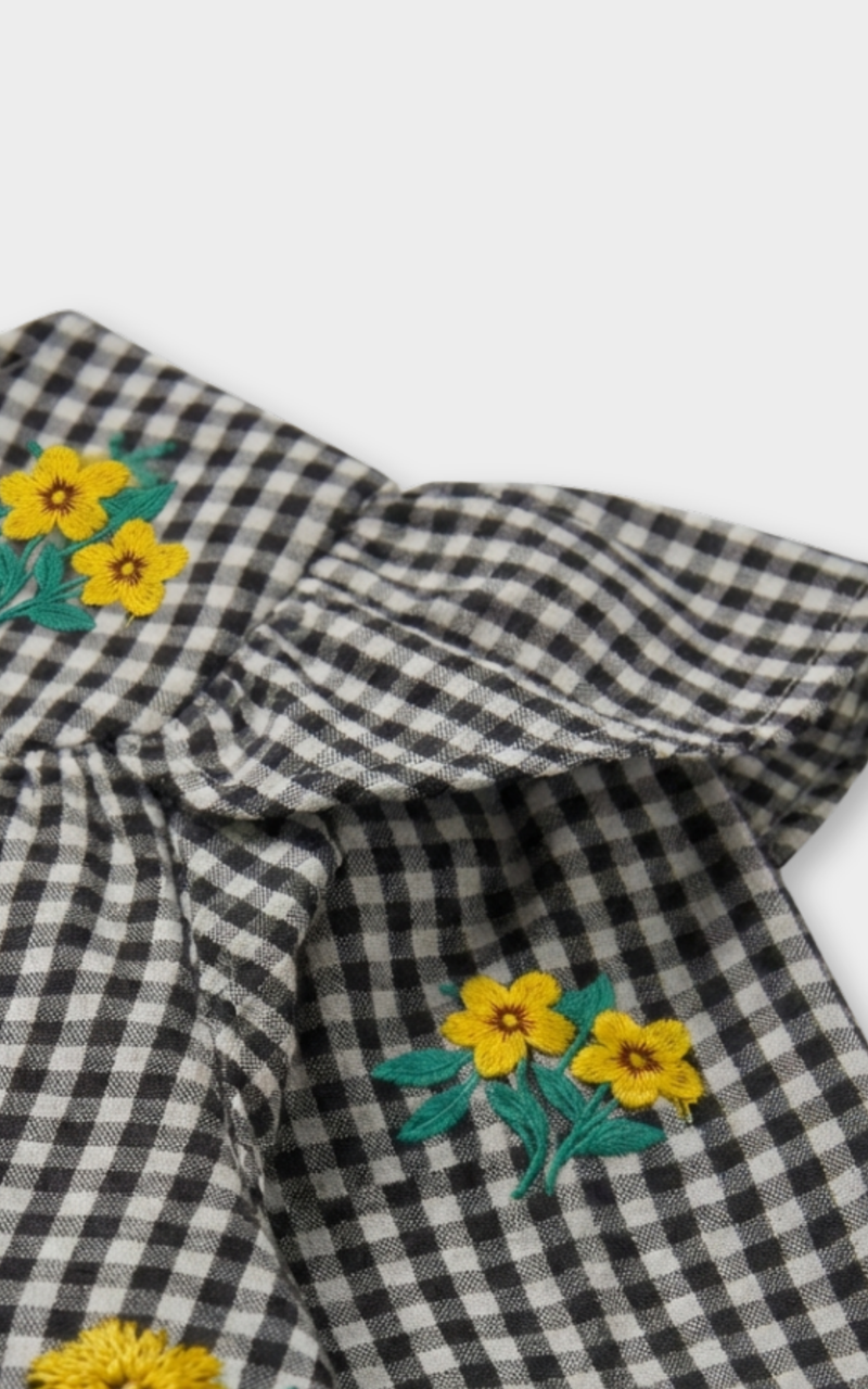 Closeup of yellow flower embroidery on black and white gingham fabric, detailed girls clothing