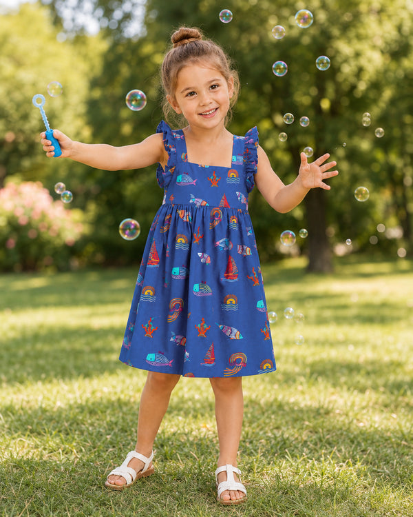 Young girl wearing a blue ocean themed dress from Kissa Ocean Collection while blowing bubbles