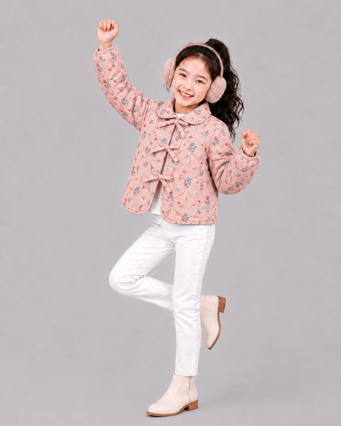 Girl dances in dusty pink floral jacket, ear muffs, and white jeans, a playful pick from coats for kids